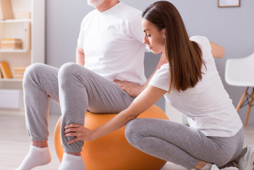Modern rehabilitation physiotherapy - women helper older man rehabilitate with an exercise ball