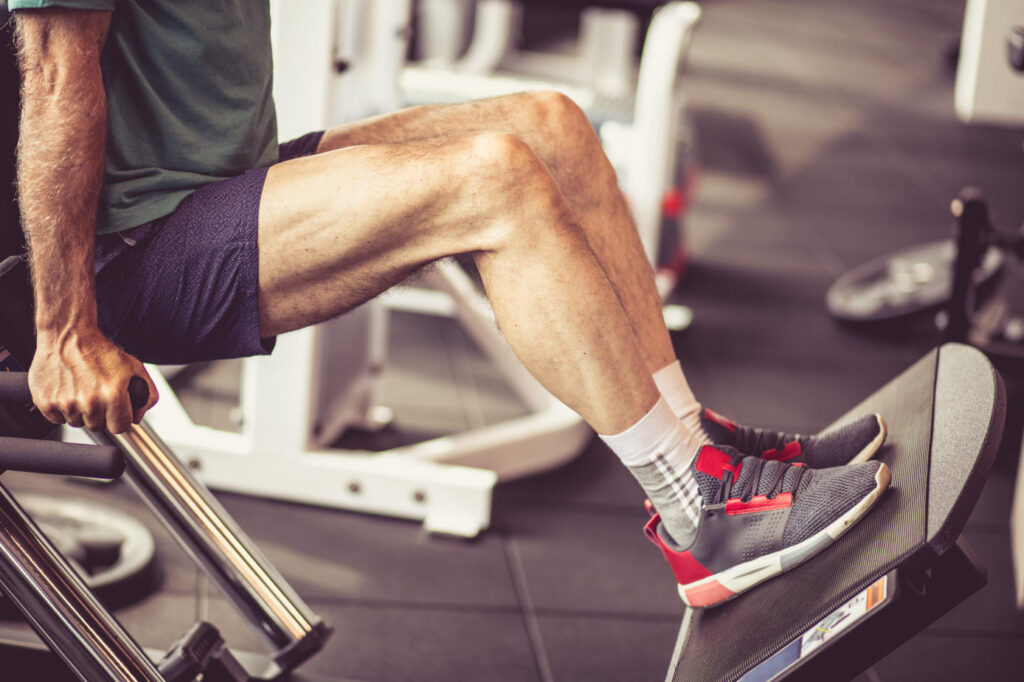 Old man working exercise on machine for legs. Close up.