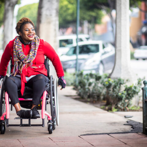 A young black disabled woman with a wheelchair and a bright colored sweater and her Asian friend walk around the city.